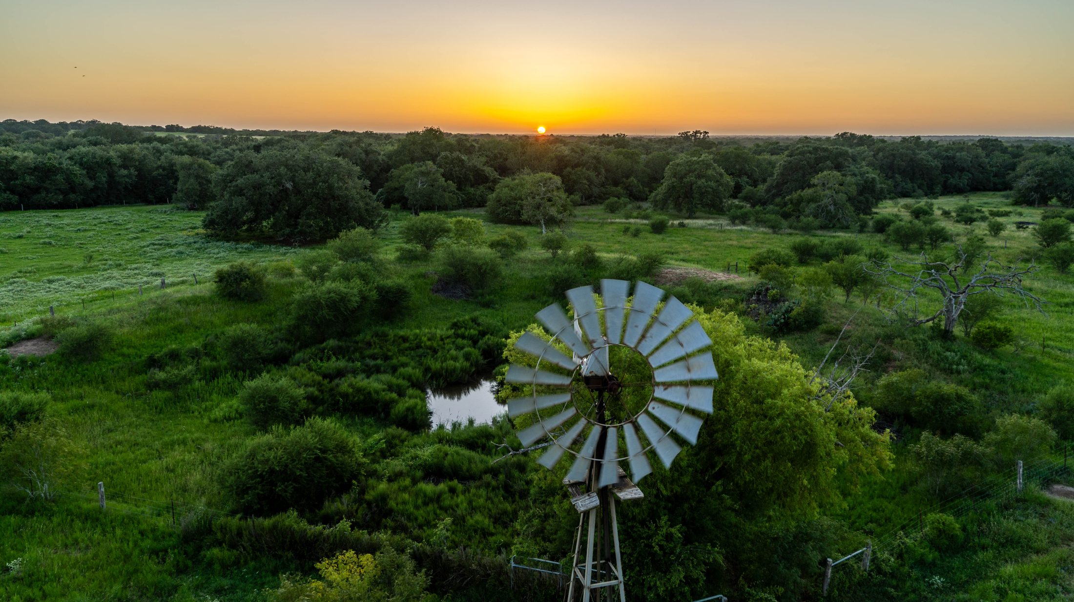 Aerial view of a working ranch in West Texas at sunset — windmill, reservoir and mesquite across an open pasture